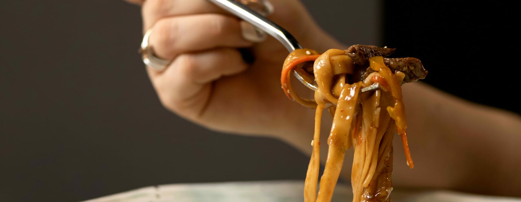 Woman eating hot pasta with fork. Italian food, noodles or spaghetti with tomato sauce on blured background. Food plate and female hand. Side view. Close-up shot. Soft focus.