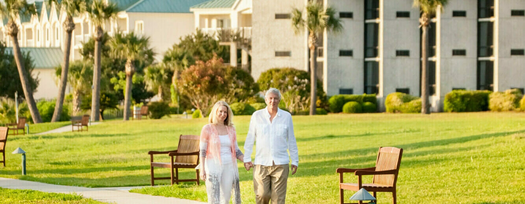 A senior couple strolls hand in hand with a retirement community in the background.