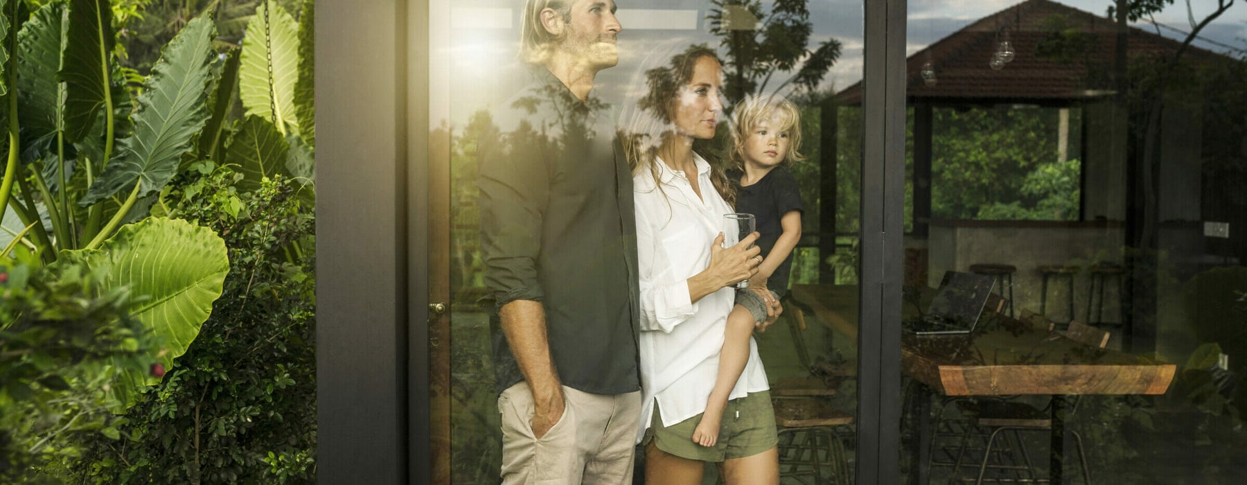 garden view of parents with their young son looking outside of their design house surrounded by lush tropical garden