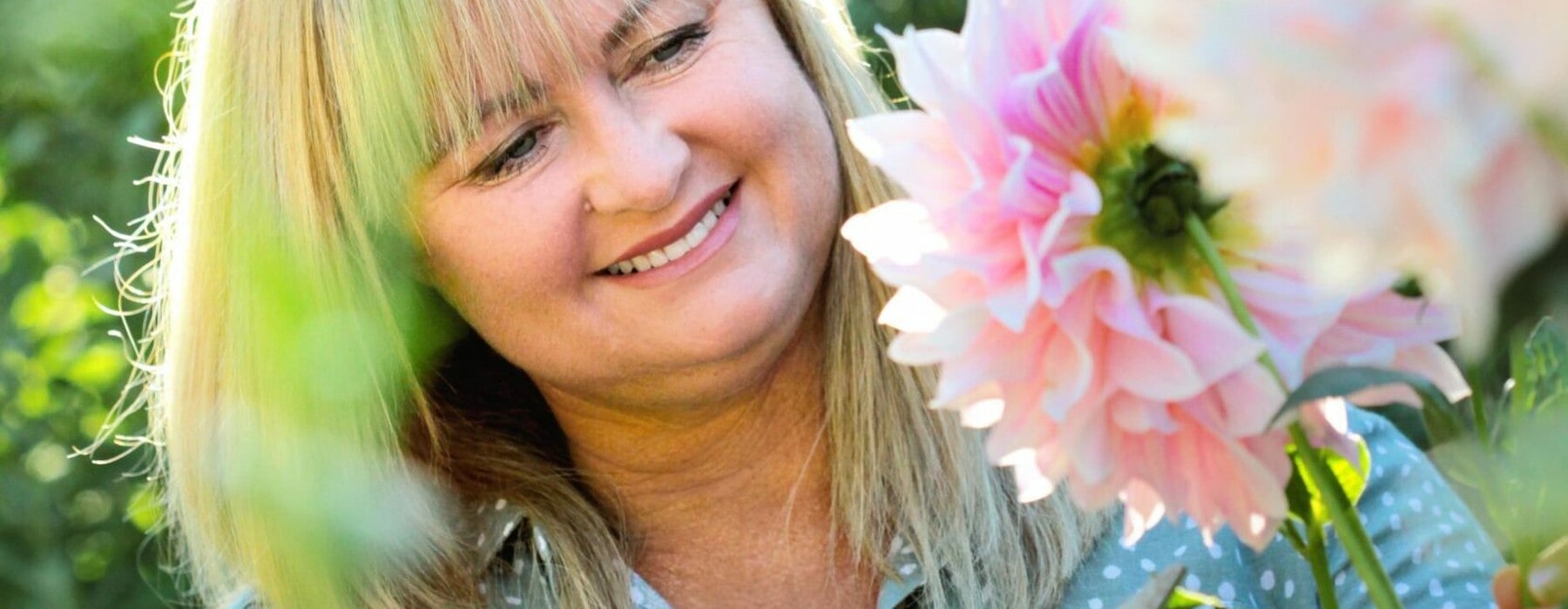Lynda Hallinan smiling while holding cutting shears in a field of dahlias