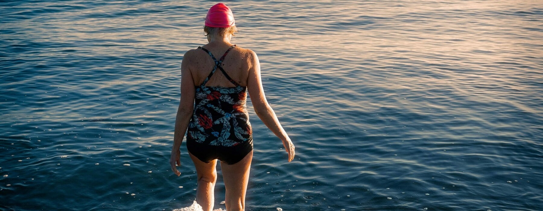 Woman wearing a swimsuit and swim crap walking away from camera in the water