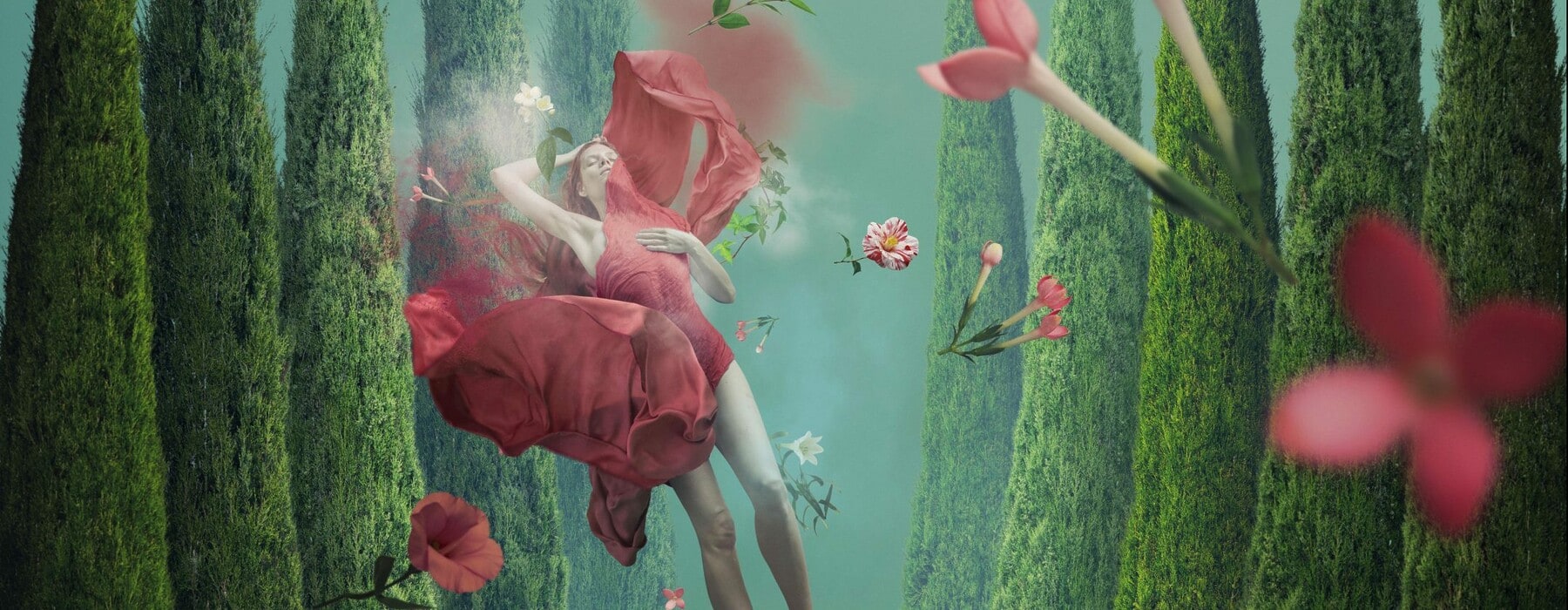 Woman wearing red dress floating in an underwater dream scene of forests and red flowers