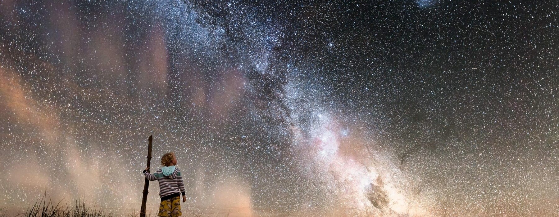 WAPFD2 Boy holding walking stick standing at beach against starry sky