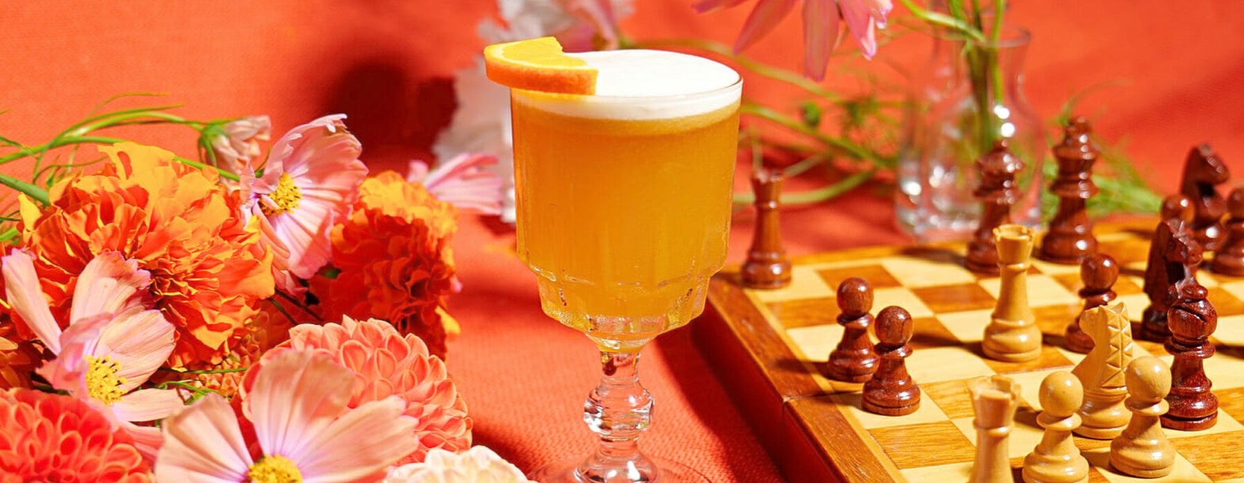 Orange rum cocktail with chessboard and flowers in front of orange backdrop