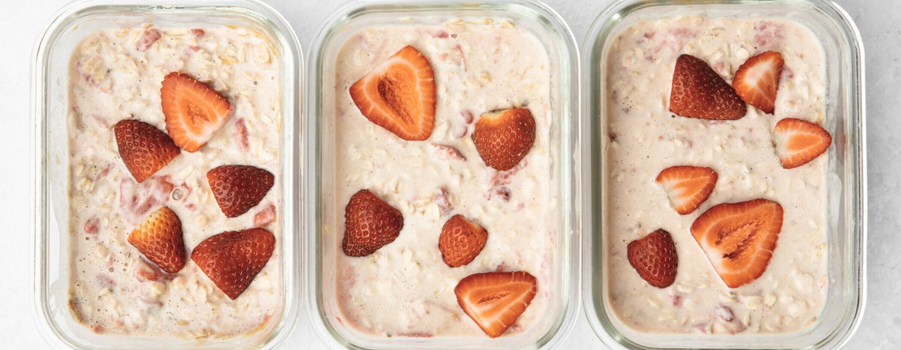 3 containers with pink coloured oats and sliced strawberries on each.
