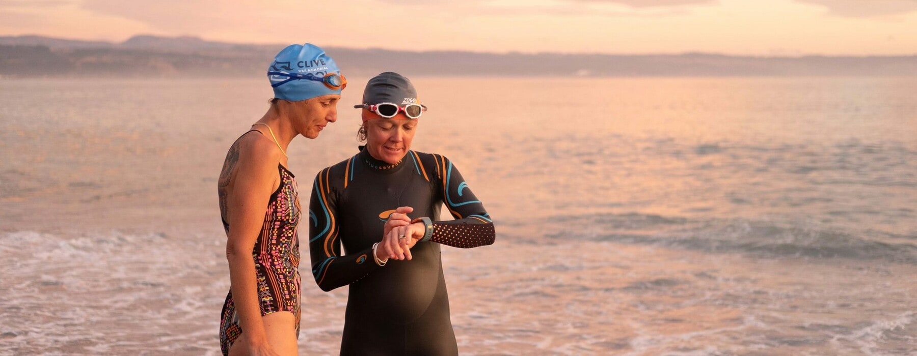 Two swimmers wearing swim suits and caps preparing to swim at the beach