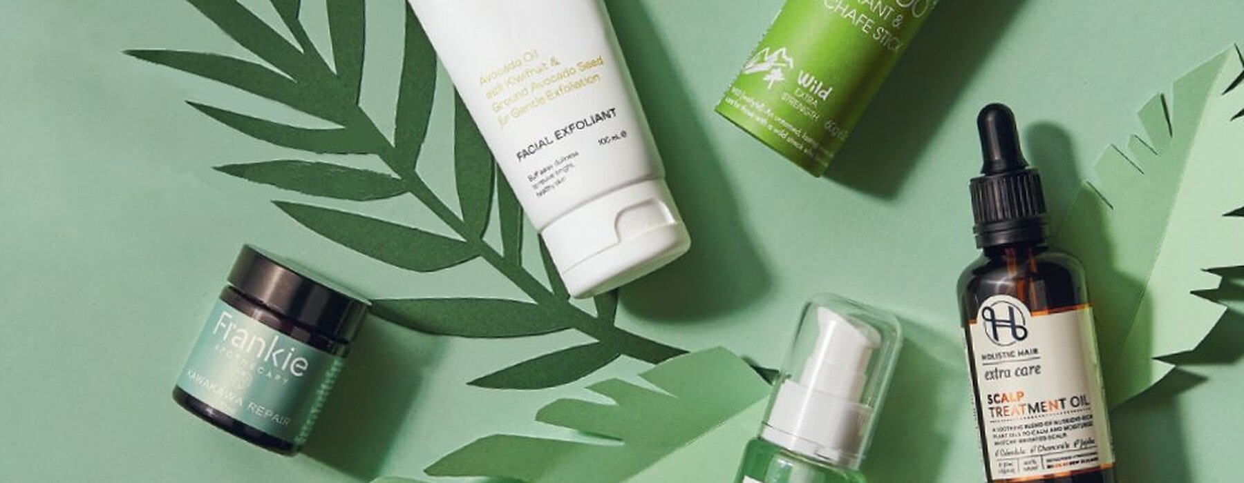 Collection of natural skincare and hair products on a green background with paper leaf cut outs