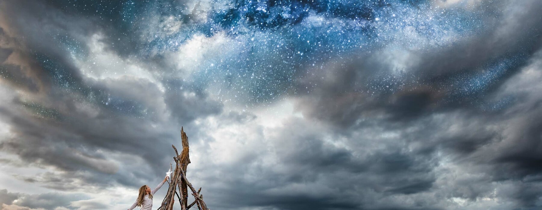 Girl placing star on driftwood tree under a starry night sky