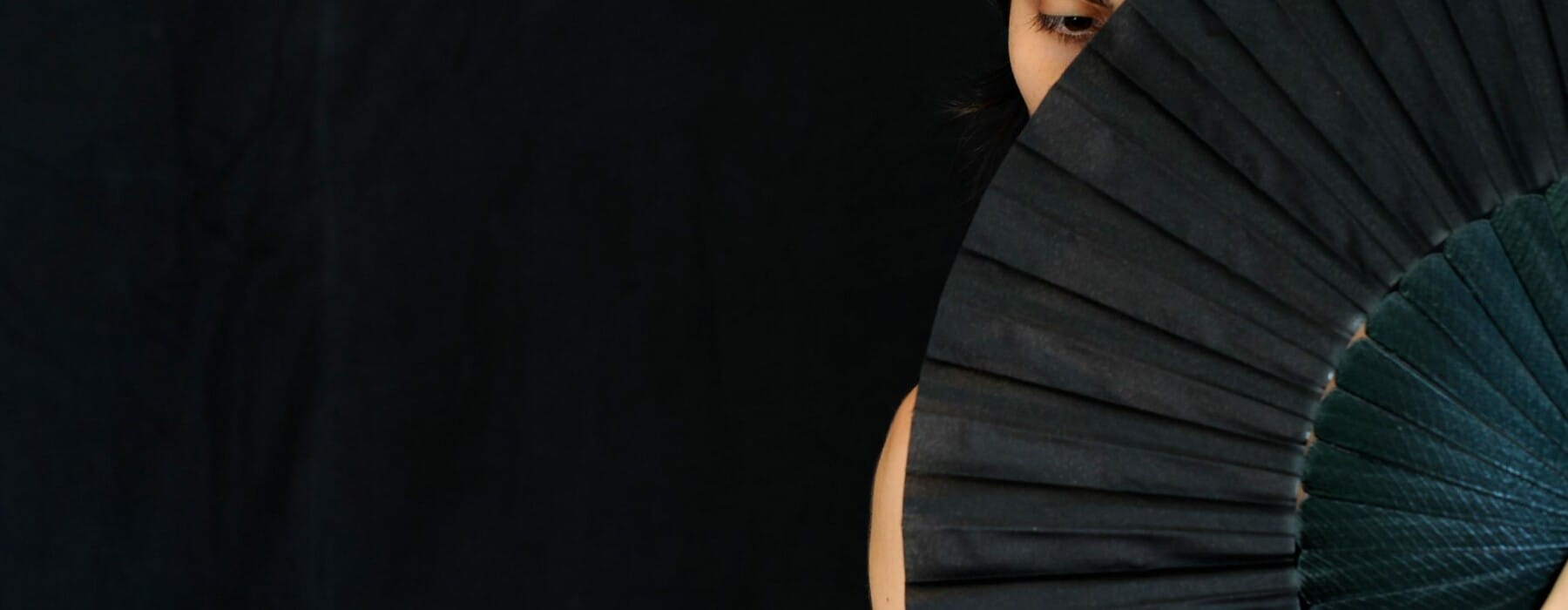 woman holding a black fan in front of her face