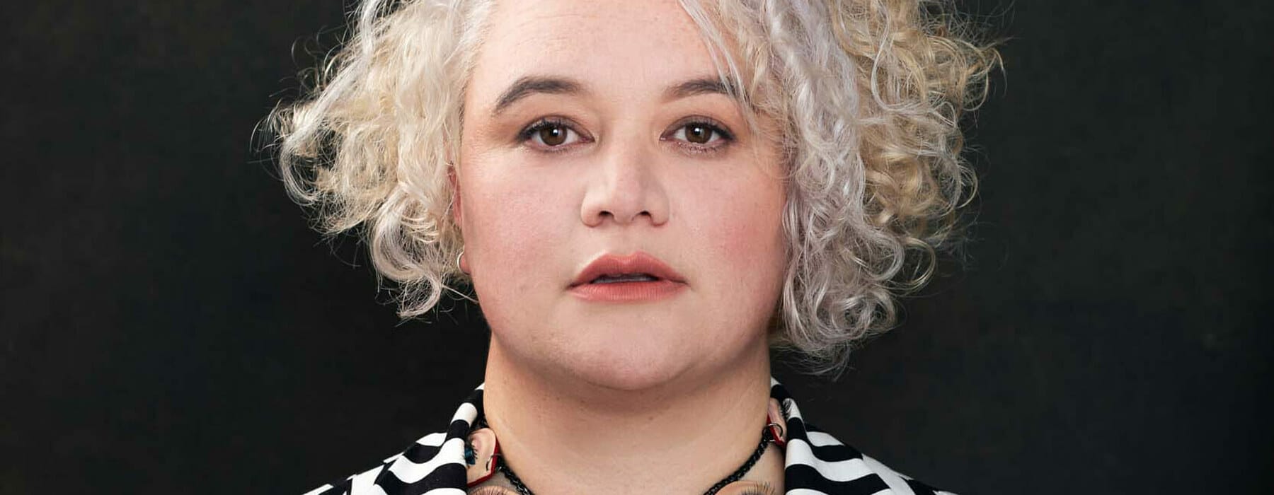 portrait of a woman wearing a black and white striped jacket with tattoos on her chest