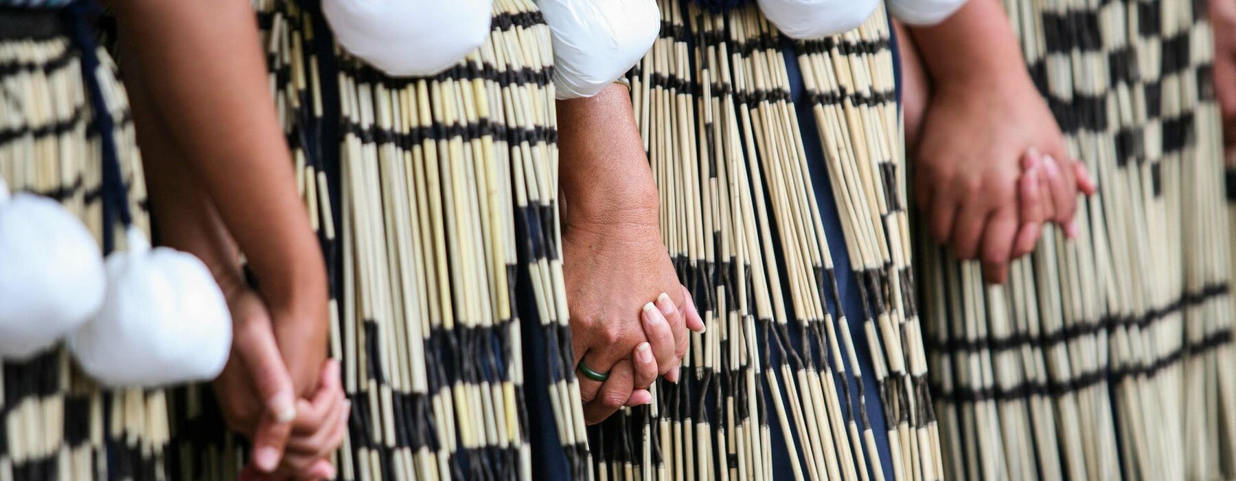 a line of people wearing piupiu and poi holding hands
