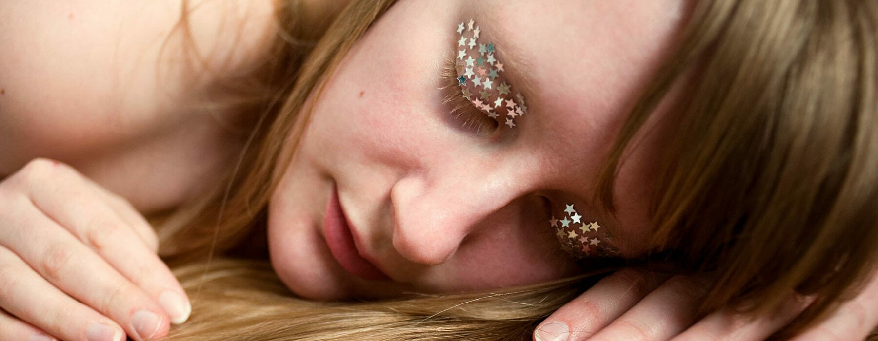 A young blonde woman laying on a silver floor. She is asleep and tiny silver stars cover her eyelids to represent dreams and dreaming.