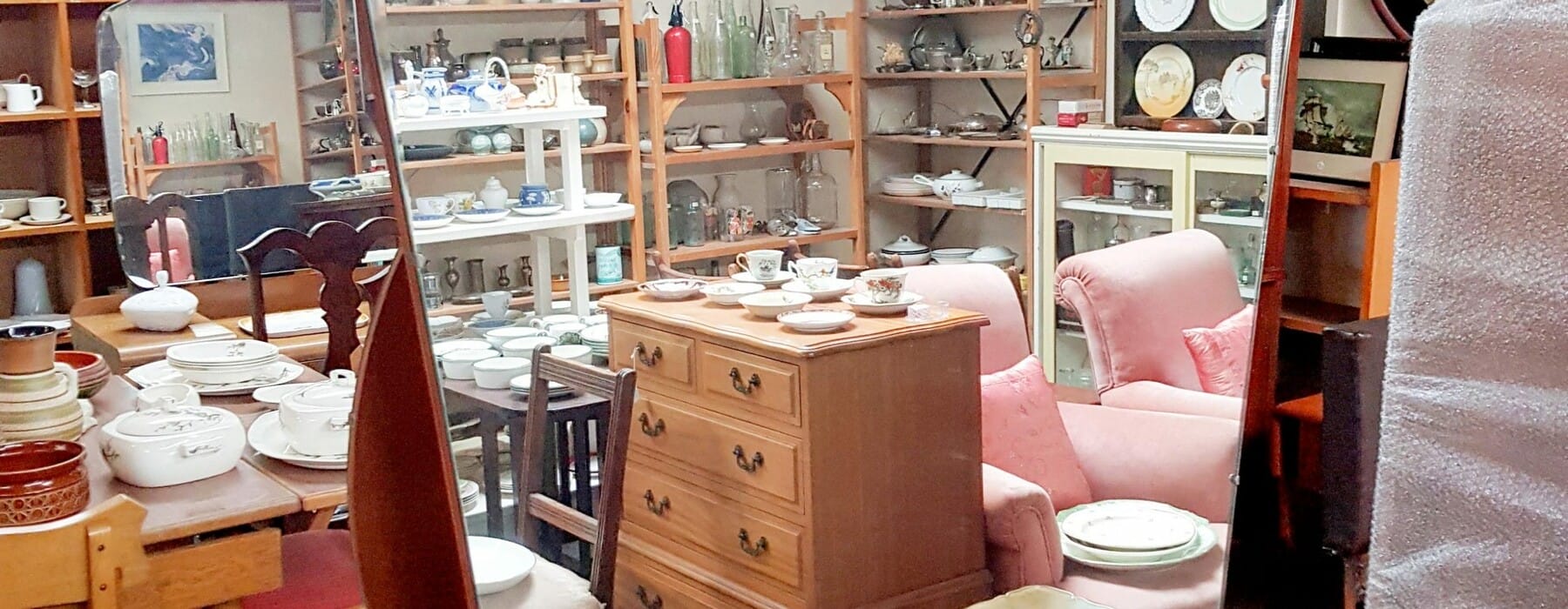 Interior of a vintage store, featuring brown wooden furniture, crockery and mirrors
